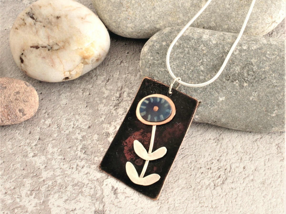 a rectangular dark red metal pendant with a silver flower