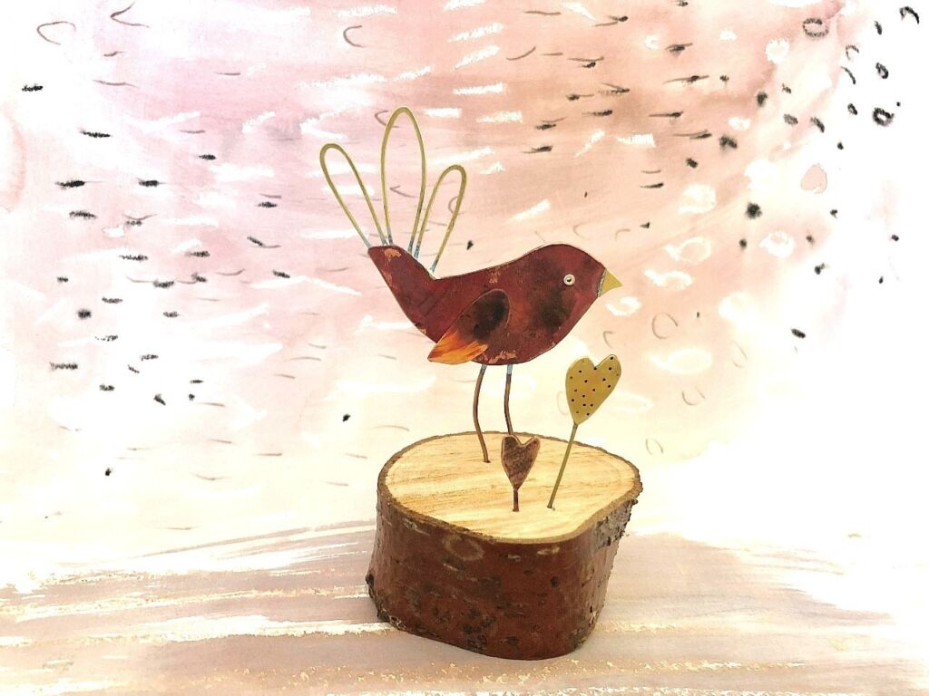 a red copper bird on a piece of wood
